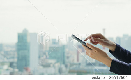 都市を背景にスマートフォンを使う女性 都市を背景にスマートフォンを使う女性 86517604