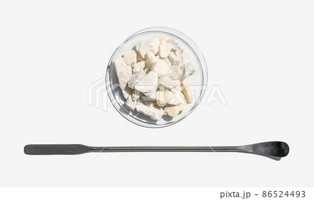 Closeup chemical ingredient on white laboratory table. Calcium carbonate Chip in Chemical Watch Glass placed next to the stainless spatula. Top View 86524493