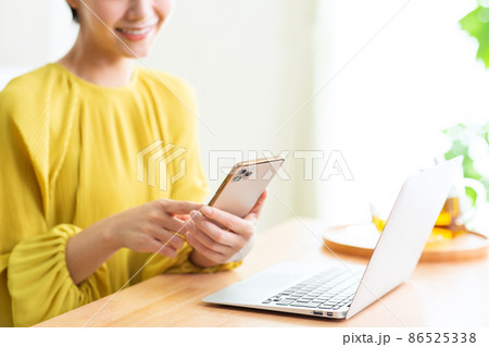リビングでパソコンとスマホをする女性　スマホ　パソコン　リビング　ライフスタイル 86525338