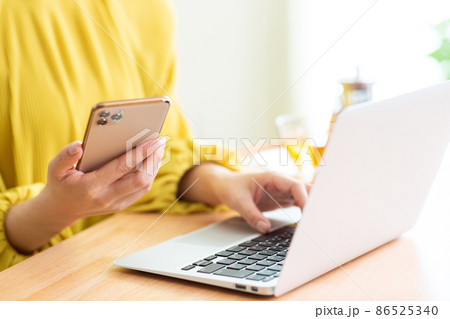 リビングでパソコンとスマホをする女性　スマホ　パソコン　リビング　ライフスタイル 86525340