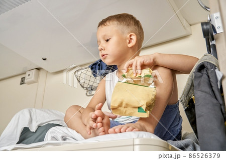 Little boy eats snacks from pack resting on top shelf in train 86526379