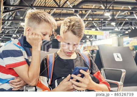 Brothers play games on phones sitting in airport hall 86526739