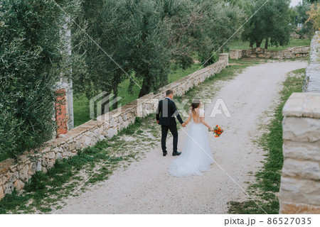 Happy stylish smiling couple walking in Tuscany, Italy on their wedding day. The bride and groom walk down the street by the hands. A stylish young couple walks. Husband and wife communicate nicely 86527035