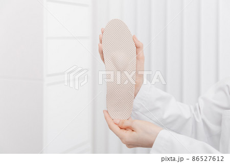 Doctor holding orthopedic insoles in his hands. Orthopedist tests the medical device. Orthopedic insoles on a white. Foot care. Flat Feet Correction. Prevention of flat feet and foot diseases. 86527612