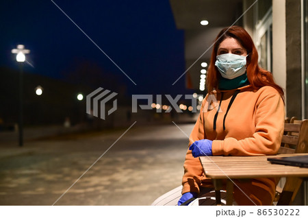 A woman in a medical mask and gloves walks late at night alone. The girl is sitting at a wooden table with a laptop in quarantine. Coronavirus. A woman in a medical mask and gloves walks late at night alone. The girl is sitting at a wooden table with a laptop in quarantine. Coronavirus. 86530222
