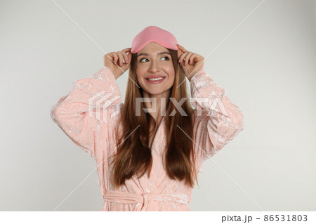 Beautiful young woman in bathrobe and eye sleeping mask on light background Beautiful young woman in bathrobe and eye sleeping mask on light background 86531803