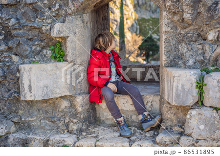 Young tourist boy enjoying a view of Kotor Bay, Montenegro. Kotor Old Town Ladder of Kotor Fortress Hiking Trail. Aerial drone view 86531895