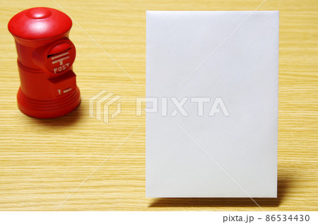 木目の机に置いた郵便ポスト形の貯金箱と郵便封筒（コピースペース有り） 86534430