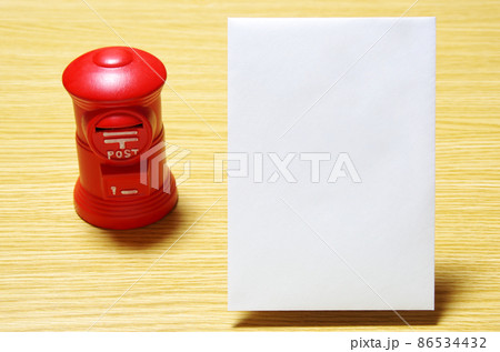 木目の机に置いた郵便ポスト形の貯金箱と郵便封筒（コピースペース有り） 86534432