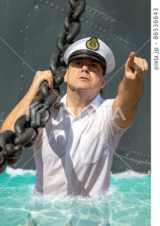 Sailor in white uniform pulls ship on coast. Captain show way for haul warship. 86536643