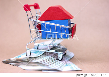 A small toy house in a supermarket cart on bundles of 1000 thousandth Russian ruble notes. The idea of buying a property. A small toy house in a supermarket cart on bundles of 1000 thousandth Russian ruble notes. The idea of buying a property. 86538167