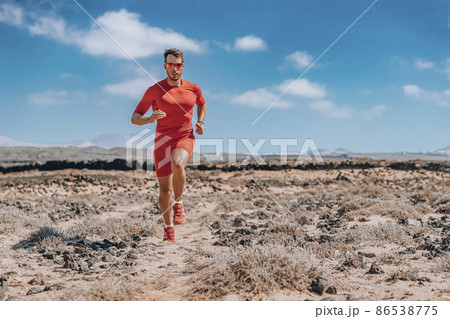 Runner ultra running man athlete wearing smartwatch, sunglasses, red compression clothes for trail run. Athlete training endurance race doing triathlon workout in desert Runner ultra running man athlete wearing smartwatch, sunglasses, red compression clothes for trail run. Athlete training endurance race doing triathlon workout in desert 86538775