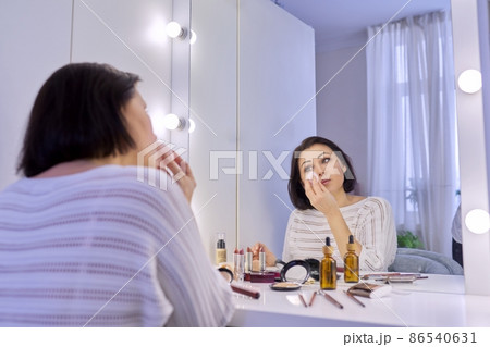 Beautiful middle aged woman doing makeup in front of a mirror. 86540631