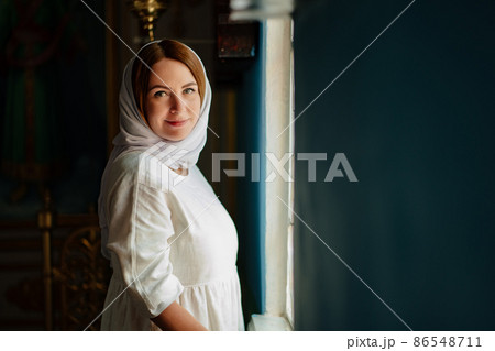 a woman in headscarf and light-colored robes by window in church.  86548711