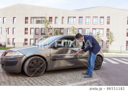 Profile of brunette man wearing jeans and jacket, car inspection for insurance claim the automobile, assesses the damage to the vehicle, examines carefully bent auto door. Outdoor shot. 86551182