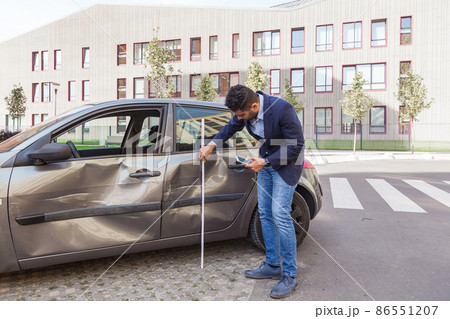 Insurance agent wearing jeans and jacket estimating car damage, assesses the damage to the automobile, dents and scratches at vehicle doors after wreck. Outdoor shot. Insurance agent wearing jeans and jacket estimating car damage, assesses the damage to the automobile, dents and scratches at vehicle doors after wreck. Outdoor shot. 86551207