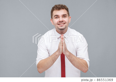 Please help me or forgive. Portrait of young hopeful man in white shirt and tie standing and looking at camera with pleased face pleading or asking for something. indoor isolated on gray background. Please help me or forgive. Portrait of young hopeful man in white shirt and tie standing and looking at camera with pleased face pleading or asking for something. indoor isolated on gray background. 86551369