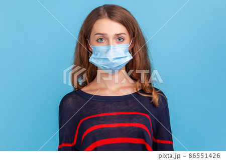 Serious woman wearing striped casual style sweater and medical mask prevent infection, airborne respiratory illness such as flu, Covid-2019. Indoor studio shot isolated on blue background. 86551426