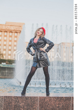Outdoor full-length portrait of young elegant woman fashion model wearing red trench cap  86557694