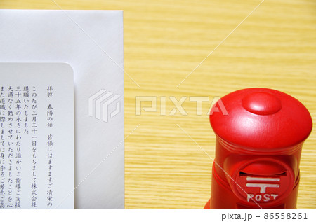 木目の机に置いた郵便ポスト形の貯金箱と礼文の封筒 86558261