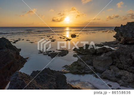 南の島の海岸で水平線に沈みゆく夕日を眺める（鹿児島県　奄美群島　沖永良部島） 86558636