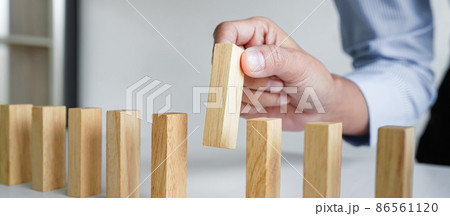 Risk and strategy in business, Close up of business woman hand gambling placing wooden block on a line of domino 86561120