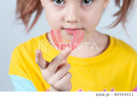 Cute little girl with blond hair is holding a pink dental myofunctional trainer 86564011