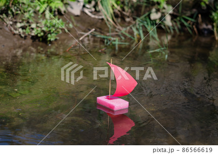 A pink sailboat floats on the pond. 86566619