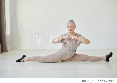 Happy mature female in light grey activewear sitting in twine 86567997