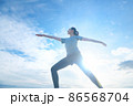 青空をバックにヨガをする若いトレーニングウェアの女性 86568704