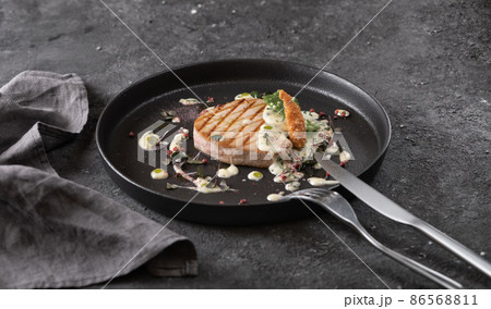 grilled tuna steak with sauce, black round plate on dark background grilled tuna steak with sauce, black round plate on dark background 86568811