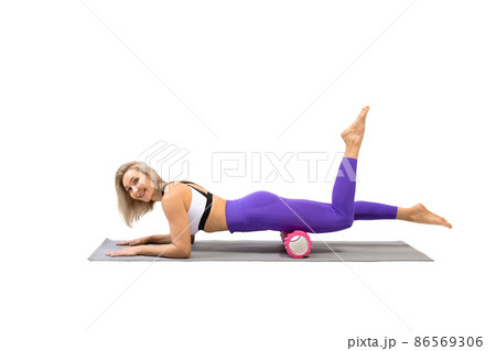 Deep self-massage with roller. Athletic smiling woman lying on front and works with her quadriceps muscles, isolated on white. 86569306