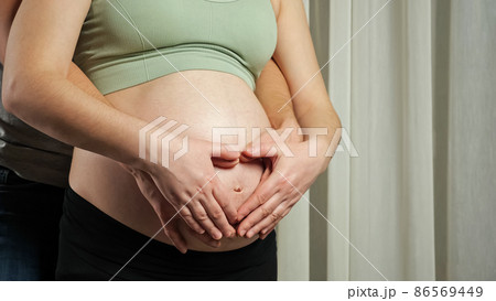 Husband and wife make heart sign hugging pregnant belly 86569449
