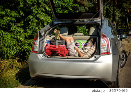 Cute little boy laying on the back of the bags and baggage in the car trunk ready to go on vacation with happy expression. Kid resting playing on smartphone Cute little boy laying on the back of the bags and baggage in the car trunk ready to go on vacation with happy expression. Kid resting playing on smartphone 86570466