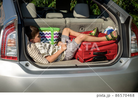 Cute little boy laying on the back of the bags and baggage in the car trunk ready to go on vacation with happy expression. Kid resting playing on smartphone Cute little boy laying on the back of the bags and baggage in the car trunk ready to go on vacation with happy expression. Kid resting playing on smartphone 86570468