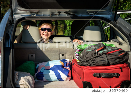 Adorable kid boy wearing sunglasses sitting in car trunk. Portrait of Happy child with open car boot while waiting for parent get ready for vocation. Family trip traveling by car concept Adorable kid boy wearing sunglasses sitting in car trunk. Portrait of Happy child with open car boot while waiting for parent get ready for vocation. Family trip traveling by car concept 86570469