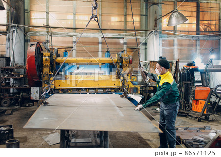 Worker lift metal sheet with crane chain hoist with remote controller and hook at industrial factory plant 86571125