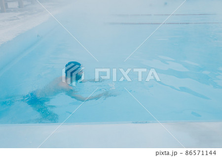 Fit swimmer male training swim in open winter swimming pool with fog. Geothermal outdoor spa health concept. Fit swimmer male training swim in open winter swimming pool with fog. Geothermal outdoor spa health concept. 86571144