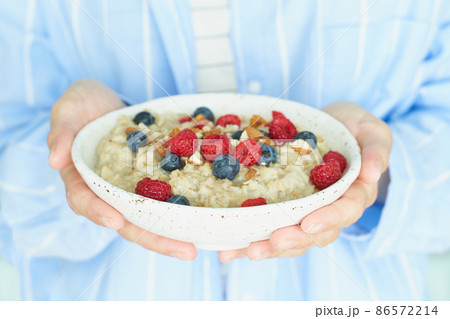 Faceless woman holds in hands breakfast, oatmeal porridge with berries and nuts Faceless woman holds in hands breakfast, oatmeal porridge with berries and nuts 86572214