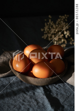 Unusual Easter on dark background. Bowl of brown eggs on dark blue table, flowers. Unusual Easter on dark background. Bowl of brown eggs on dark blue table, flowers. 86572288