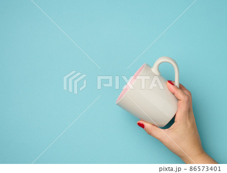 female hand holds a ceramic mug on a blue background, break time and drink coffee female hand holds a ceramic mug on a blue background, break time and drink coffee 86573401
