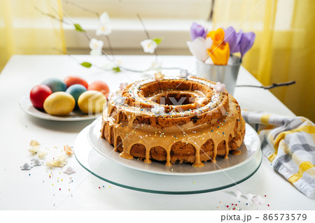 Delicious Easter cake on kitchen table with colored eggs and handmade paper flowers. Easter breakfast. Holidays concept Delicious Easter cake on kitchen table with colored eggs and handmade paper flowers. Easter breakfast. Holidays concept 86573579