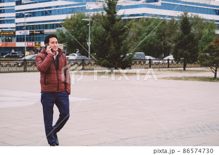 asian man walking in the street with phone. asian man walking in the street with phone. 86574730