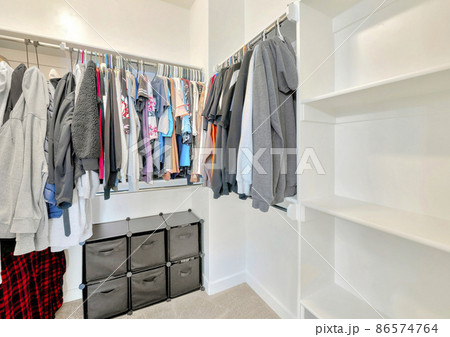 Small walk-in closet with hanging sweaters, shirts and blouse on the metal rods 86574764