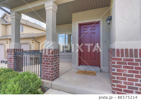Red front door of a house with red bricks siding and railings at the porch 86575214