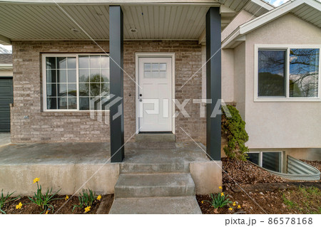 Porch of a house with black column posts and white front door with glass panel 86578168
