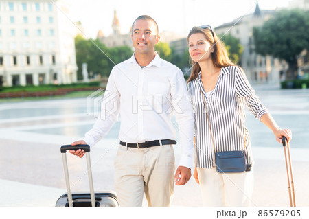 Woman and man travelers walking with baggage through city Woman and man travelers walking with baggage through city 86579205