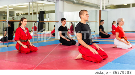 Man in red and black martial arts uniform sitting on mat in gym 86579588