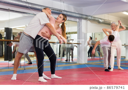 Young woman with male partner practicing basic elbow kick to chin during back grab Young woman with male partner practicing basic elbow kick to chin during back grab 86579741