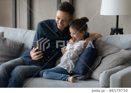 Joyful young caring father and adorable small daughter using cellphone. Joyful young caring father and adorable small daughter using cellphone. 86579750